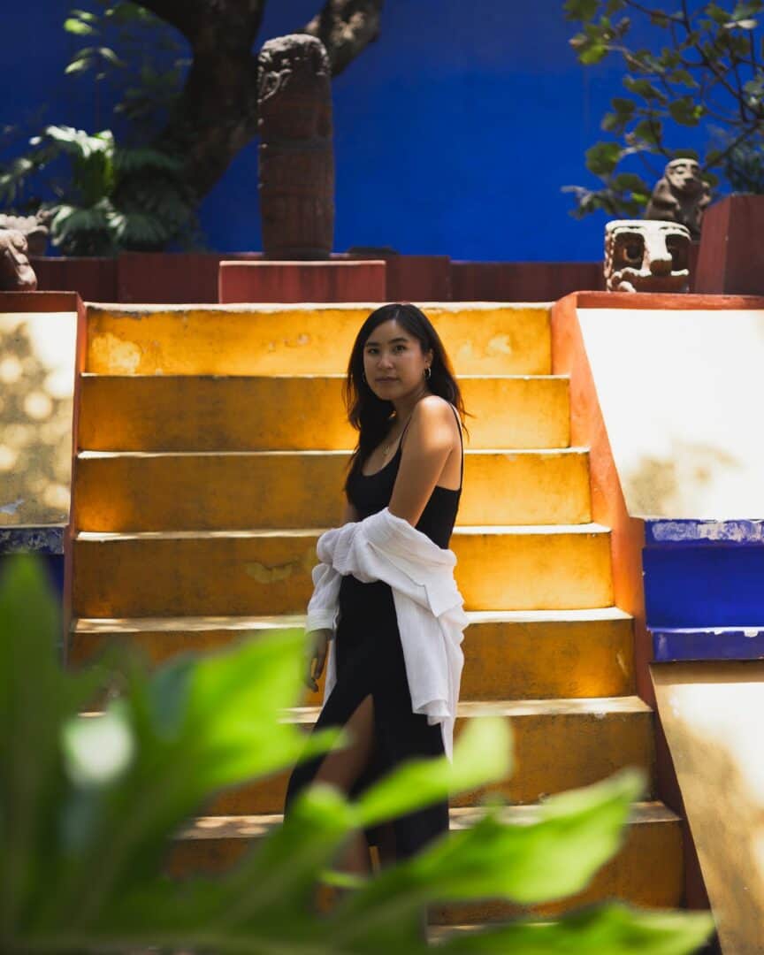 Chloe posing for an Instagram photo in front of a yellow stairs at Museo de Frida Kahlo in Mexico City