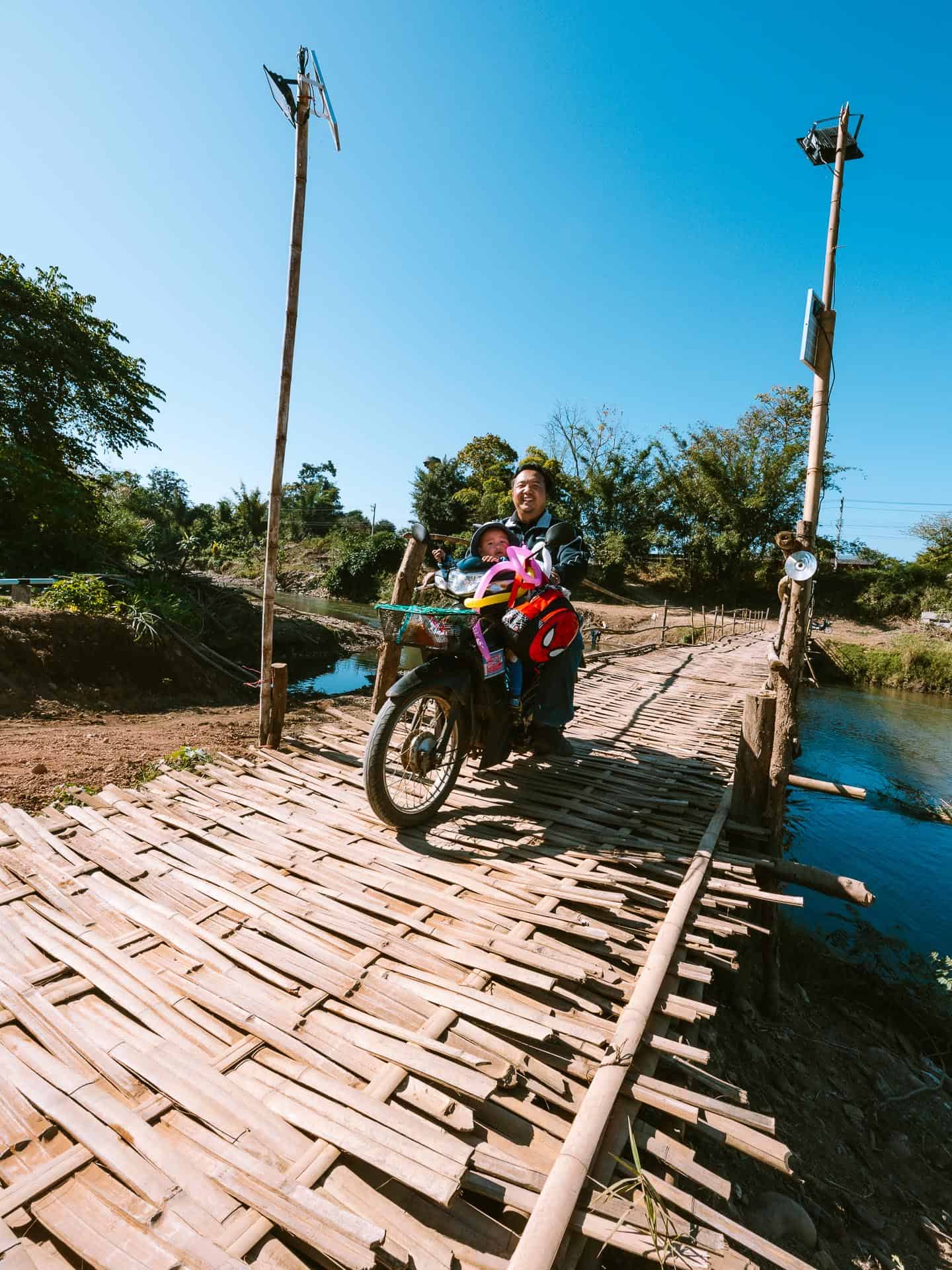 Man and child motorbiking across bamboo bridge in Pai, Thailand